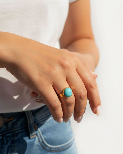 Hand wearing a gold waterproof adjustable band ring with a vibrant turquoise stone