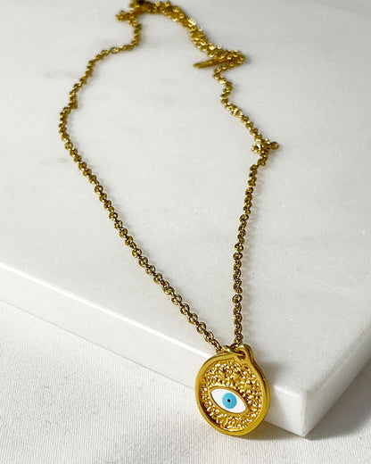A dainty chain necklace with a small round pendant. The pendant is gold with a white blue enamel evil eye design.