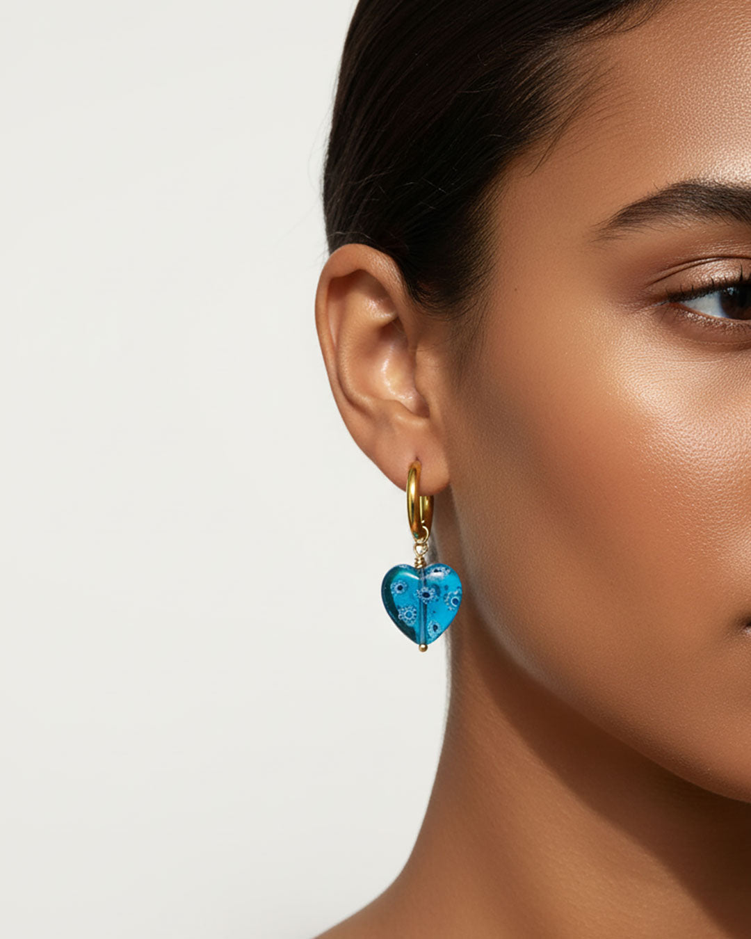 Model wearing gold hoop earrings with blue heart charm