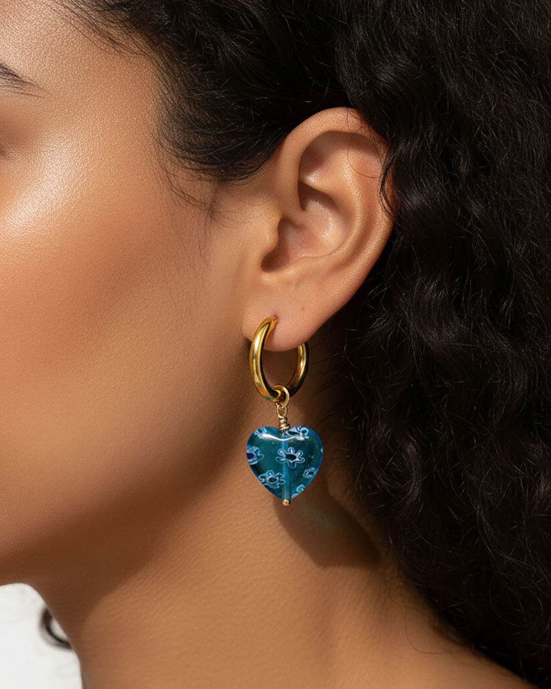 Model wearing gold hoop earrings with blue heart charm