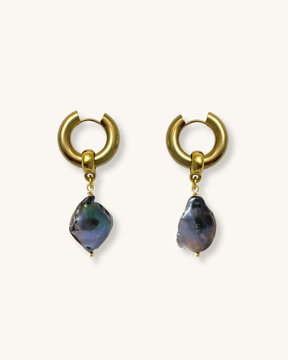 The Black Baroque Pearl Hoops, a pair of gold stainless steel hoop earrings adorned with irregular-shaped black pearls.
