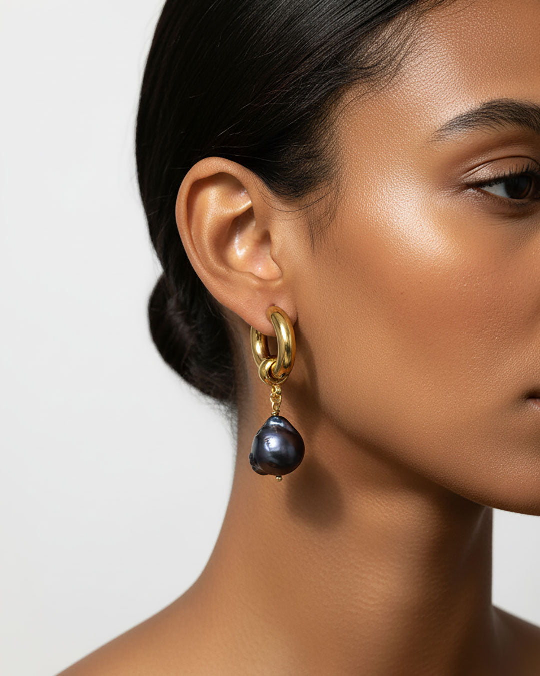Model wearing a pair of gold stainless steel hoop earrings adorned with irregular-shaped black pearls.