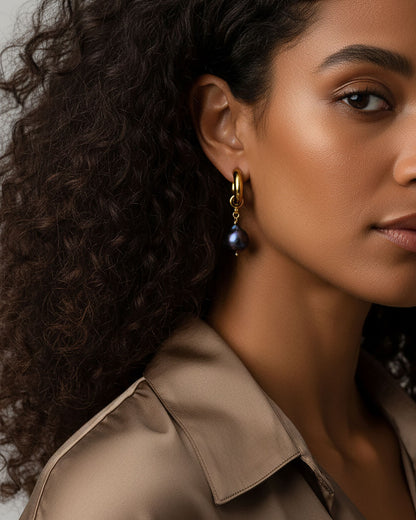 Model wearing a pair of gold stainless steel hoop earrings adorned with irregular-shaped black pearls.