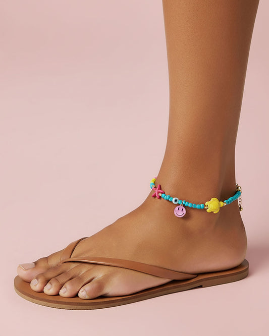 Colorful beaded anklets on a foot wearing a sandal against a pink background