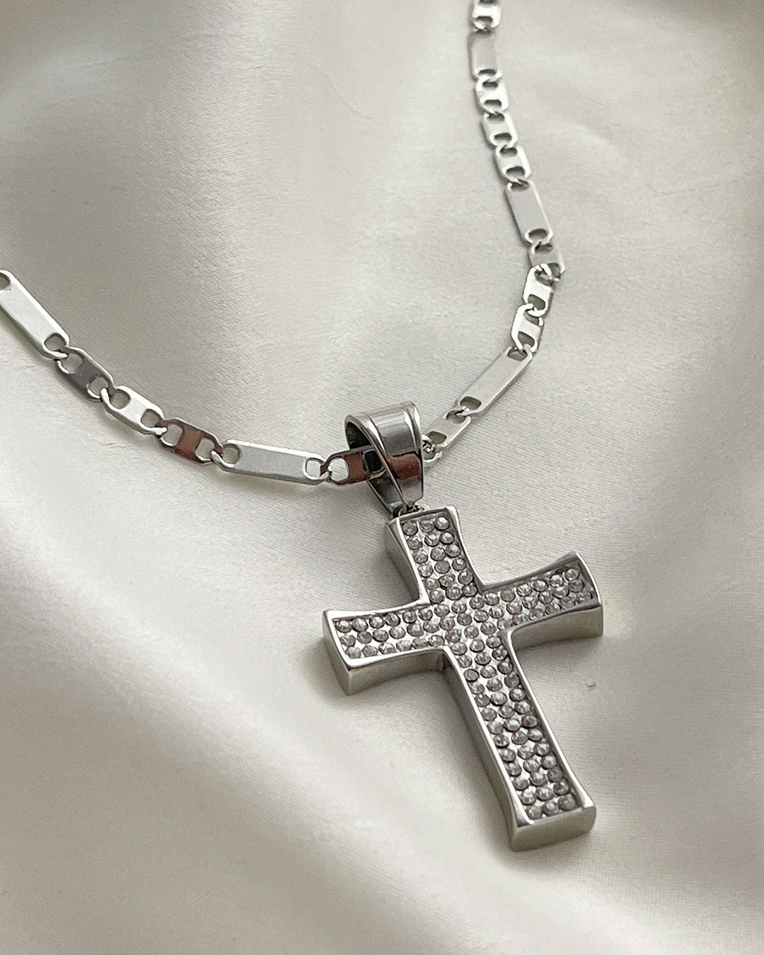 A silver chain necklace with a silver cross pendant. The cross is encrusted with small, clear cubic zirconia stones.