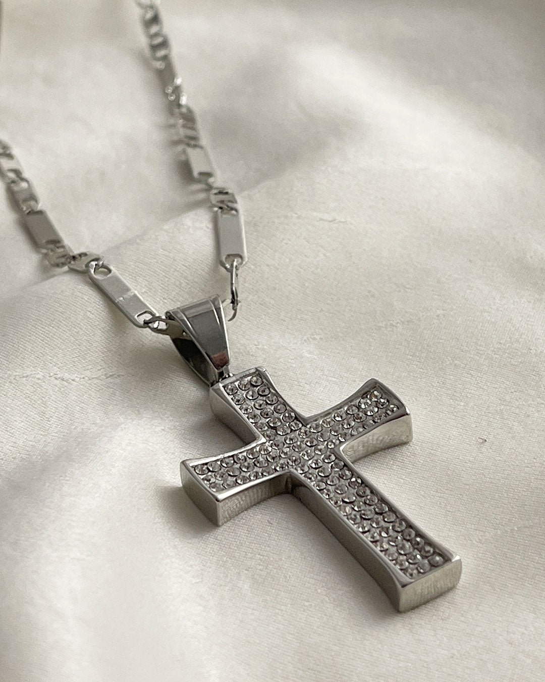 A silver chain necklace with a silver cross pendant. The cross is encrusted with small, clear cubic zirconia stones.