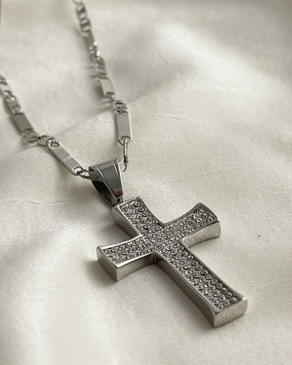 A silver chain necklace with a silver cross pendant. The cross is encrusted with small, clear cubic zirconia stones.