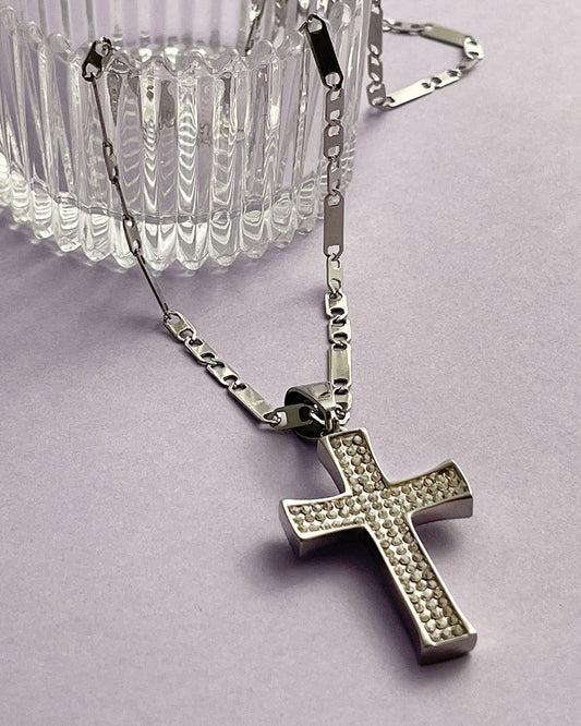 A silver chain necklace with a silver cross pendant. The cross is encrusted with small, clear cubic zirconia stones.