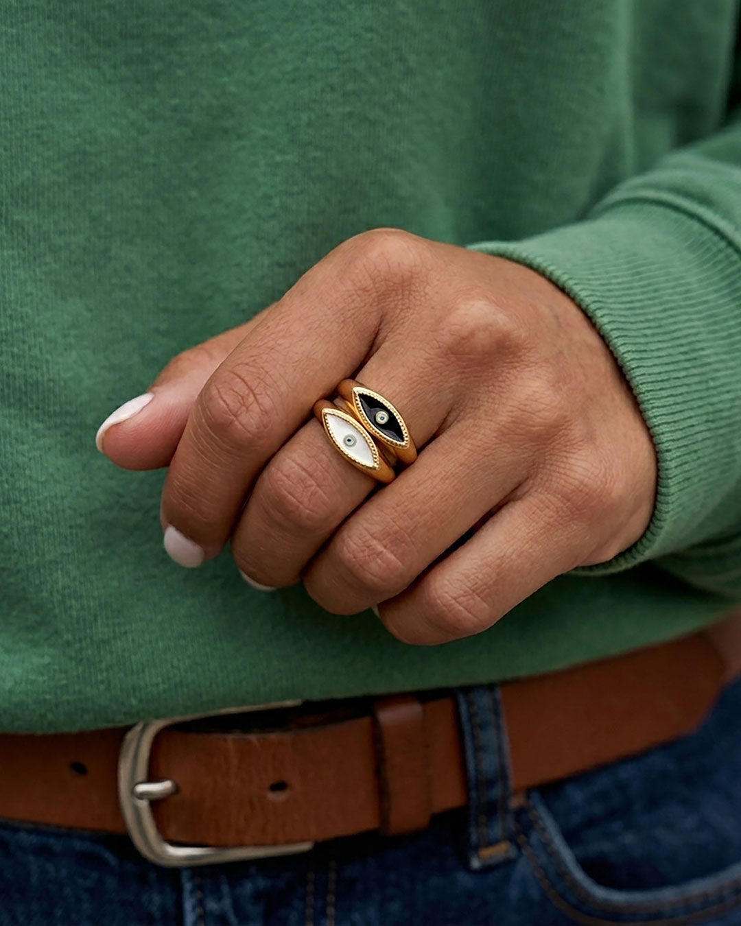 Two gold rings featuring an eye-shaped design with white and black enamel in the center on a woman's finger.