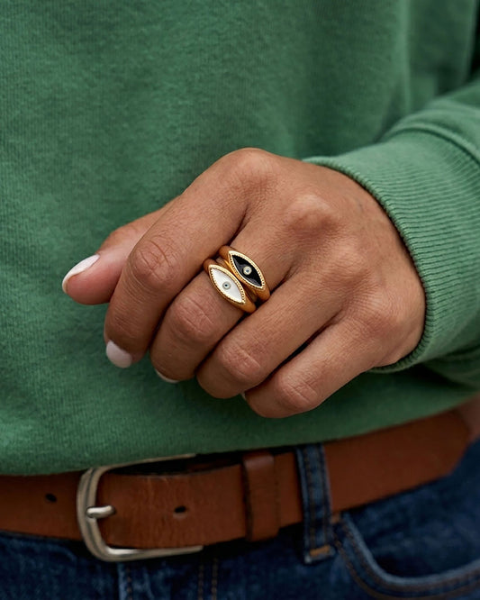 Two gold rings featuring an eye-shaped design with white and black enamel in the center on a woman's finger.
