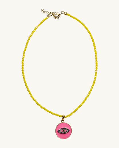 A yellow beaded necklace with a fuchsia round eye pendant.