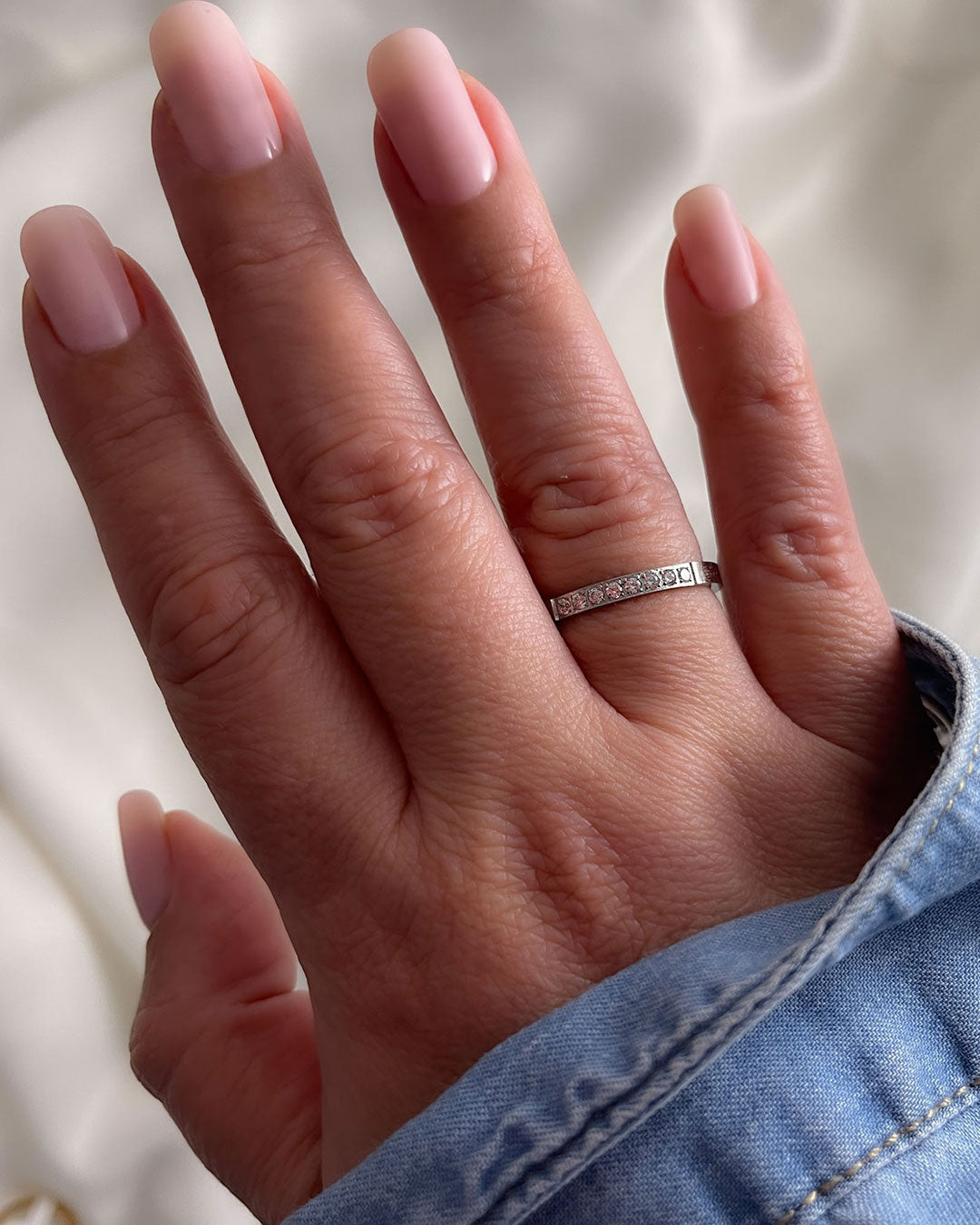 A woman’s hand wearing a silver band ring with diamonds on a neutral background