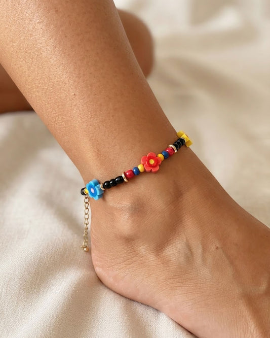 A black glass beaded anklet adorned with colorful daisy flower beads on a foot