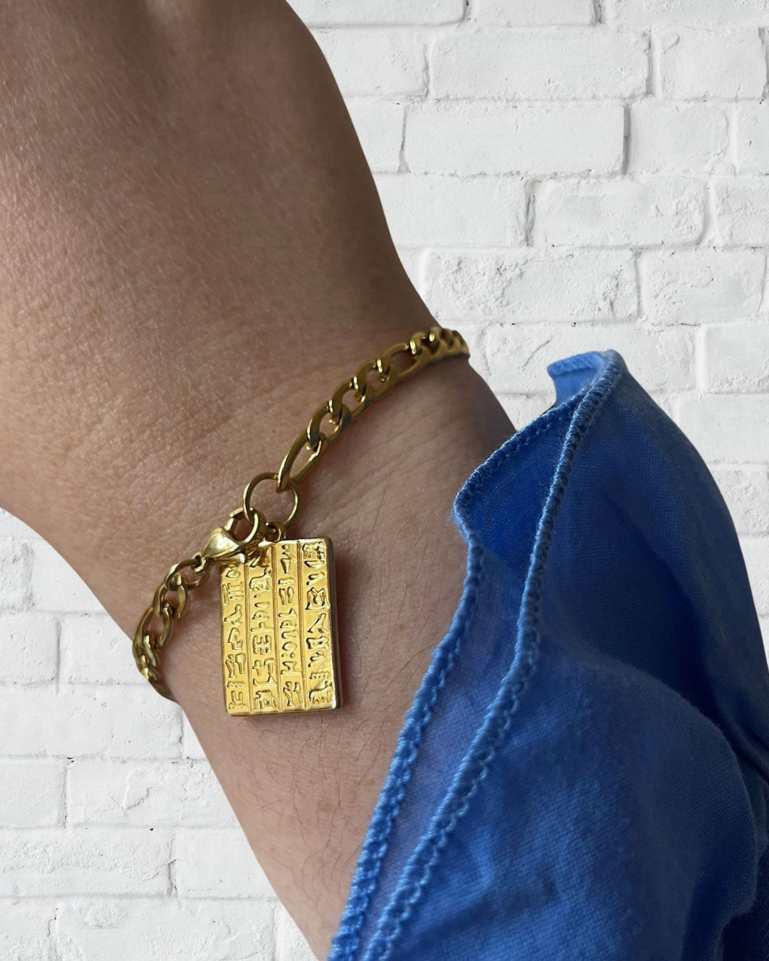 An Egyptian style chain bracelet with a tag charm in gold on a wrist
