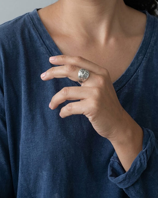 A close-up of a woman's hand wearing a silver floral dome ring