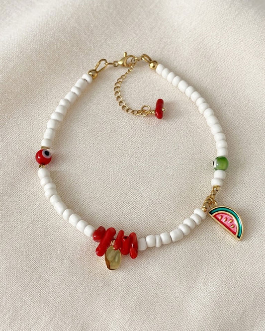 A white glass beaded anklet adorned with a watermelon charm and coral shell beads