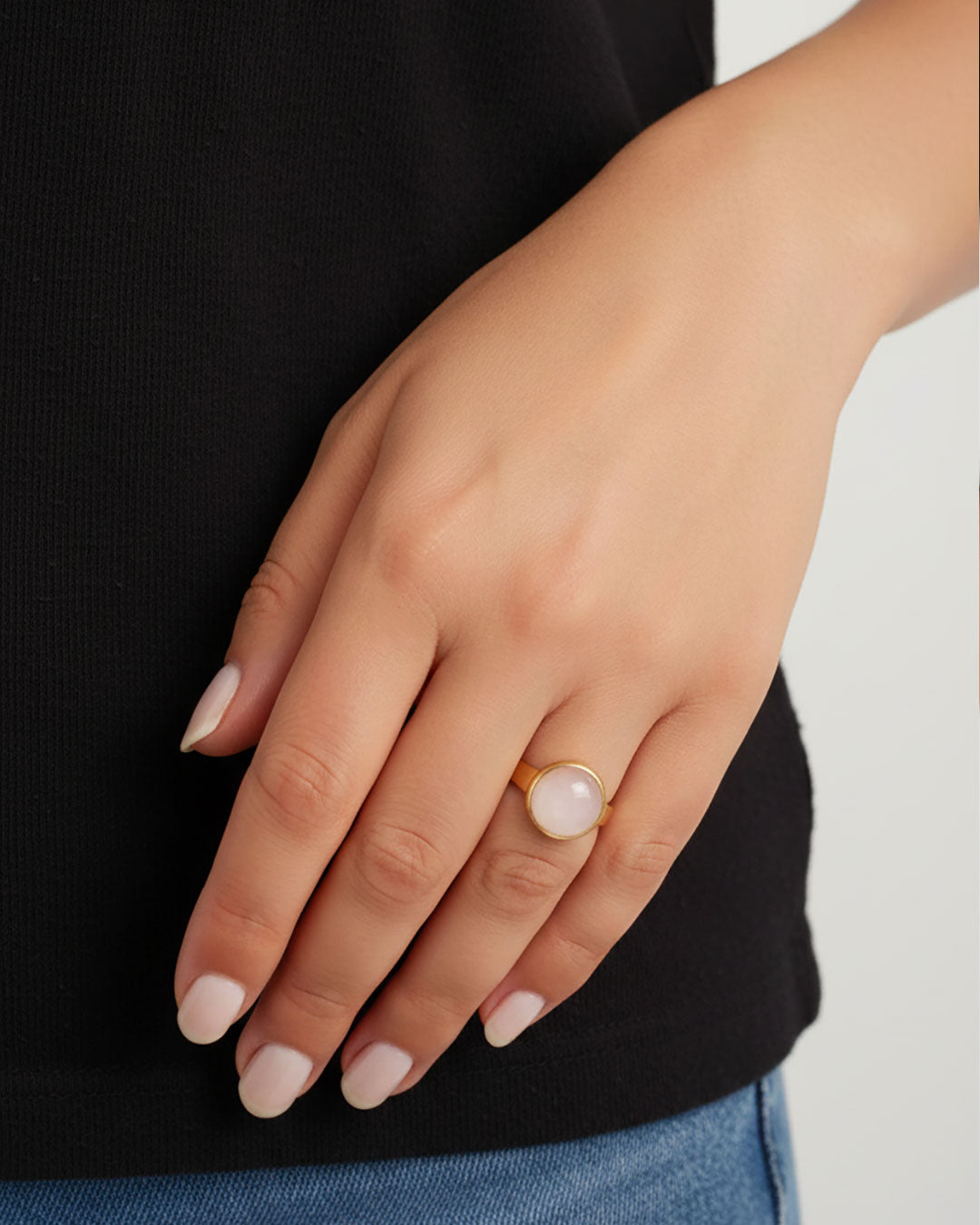 Hand wearing a gold waterproof adjustable band ring with a rose quartz stone