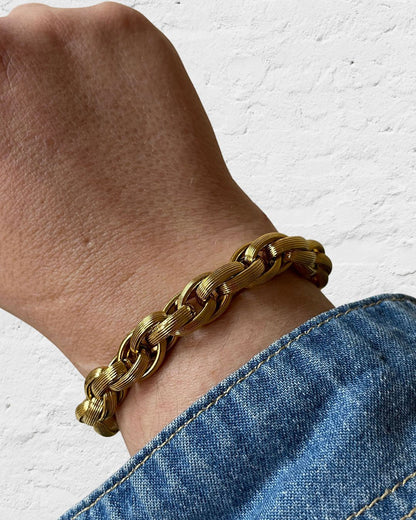 A gold chain bracelet with a large, round, gold coin charm. The coin has a raised design of Athena's goddess face. 