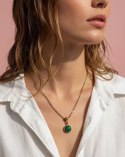 Close-up of a woman wearing a gold necklace with an aventurine pendant against a pink background