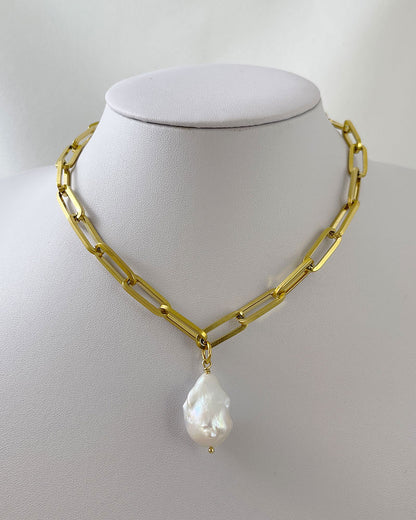 A gold chunky chain necklace with a large baroque pearl in the middle