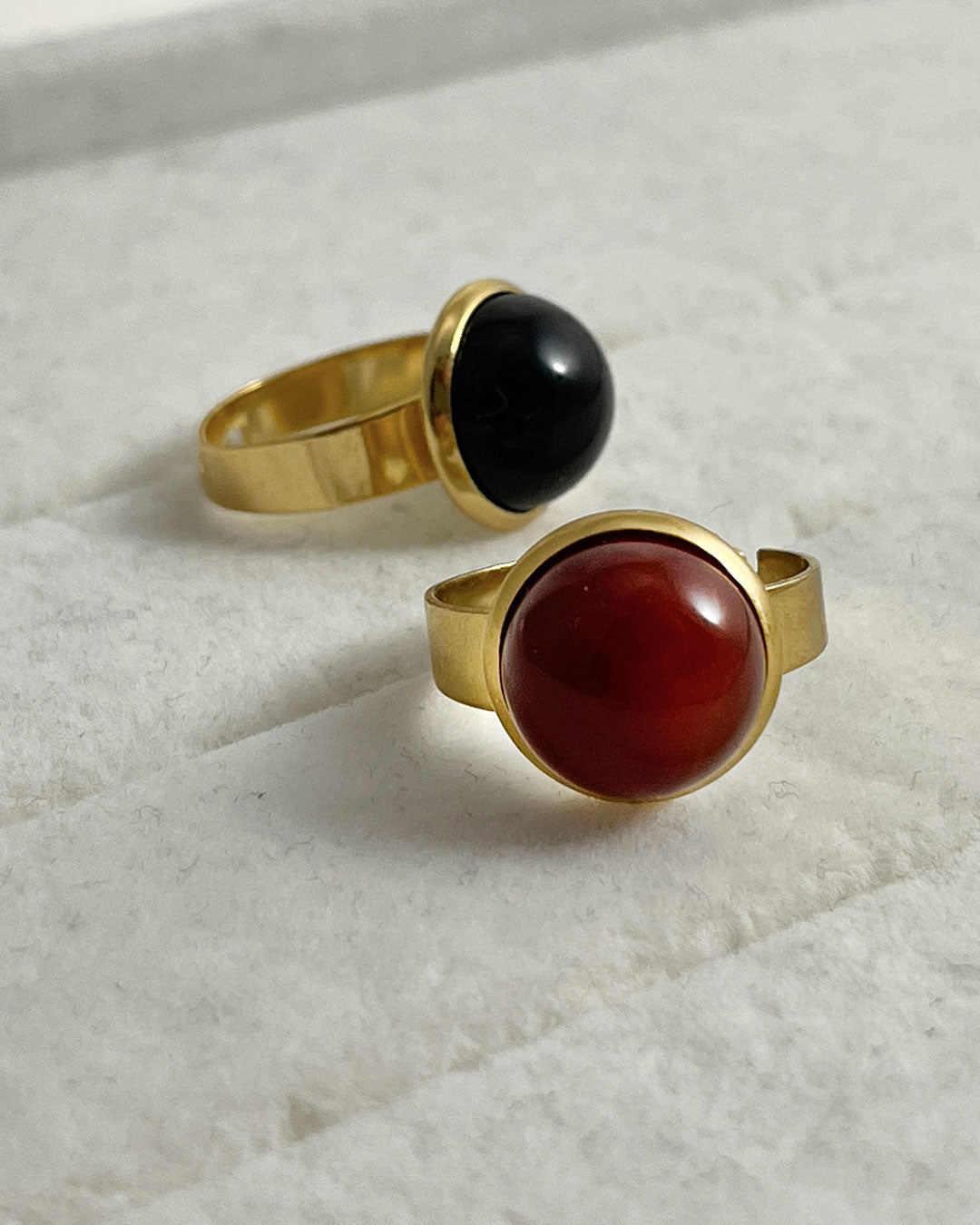 Two rings with red carnelian and black onyx gemstones on a light background