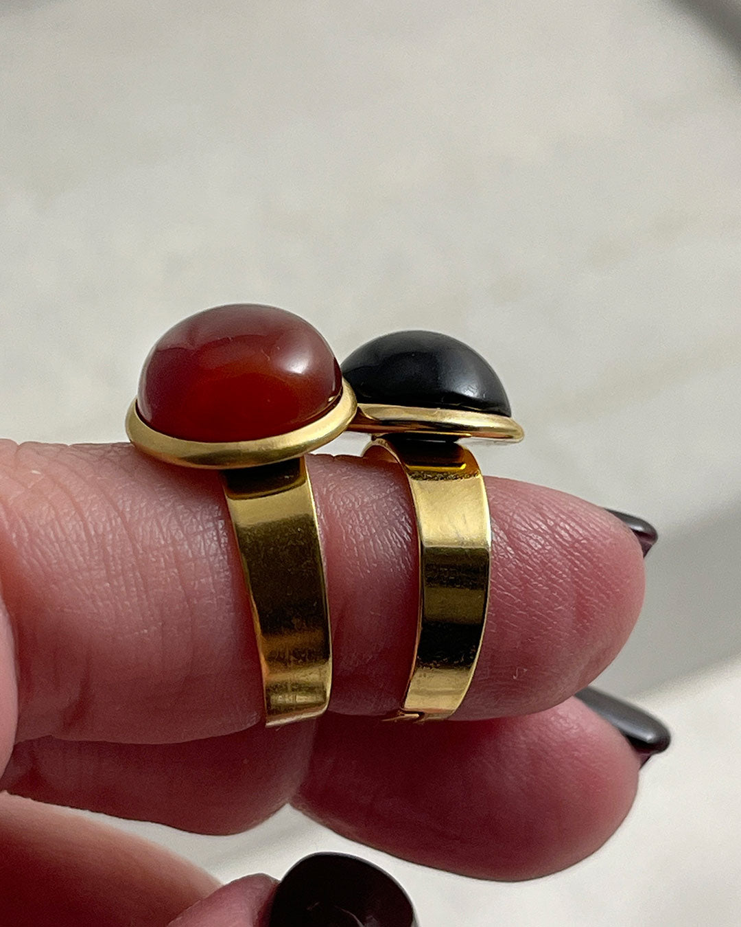 Two rings with red carnelian and black onyx gemstones on a light background
