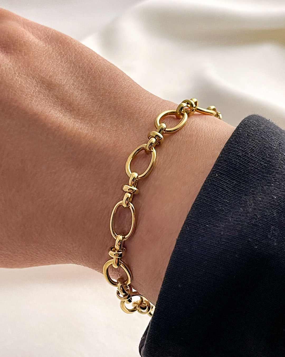 Gold oval link chain bracelet on a wrist with a neutral background