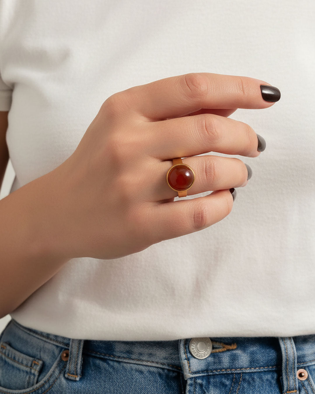 Hand wearing a gold ring with a carnelian gemstone against a neutral background