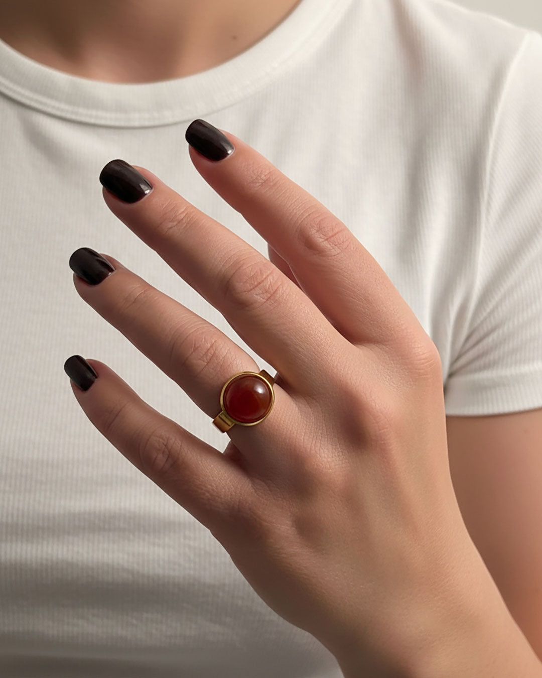 Hand wearing a gold ring with a carnelian gemstone against a neutral background