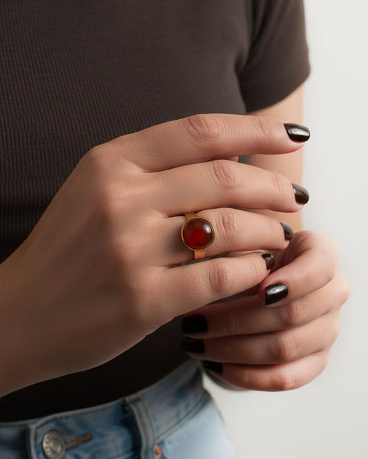 Hand wearing a gold ring with a carnelian gemstone against a neutral background
