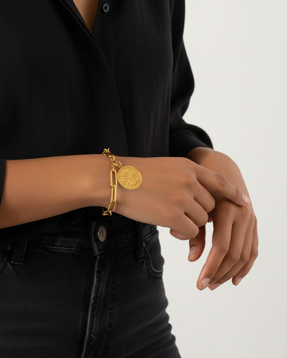 Gold bracelet with a decorative coin charm on a wrist
