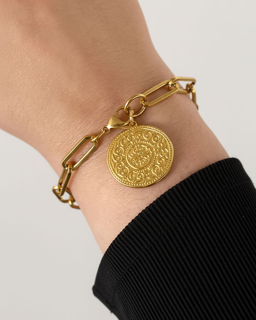 Gold bracelet with a decorative coin charm on a wrist against a neutral background