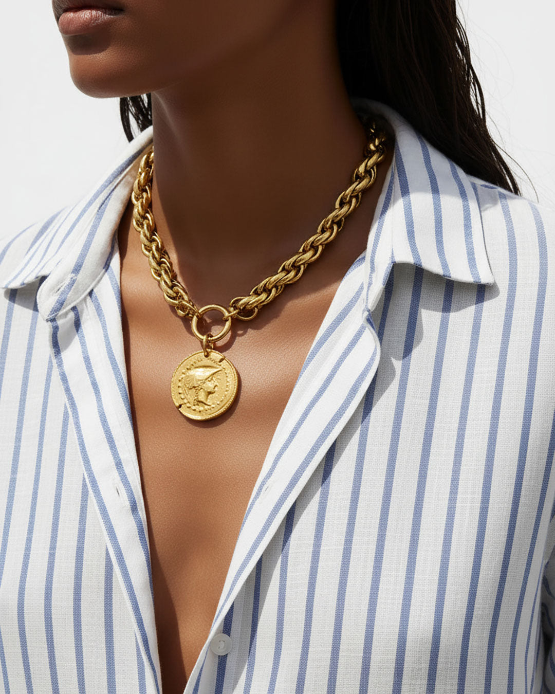 Model wearing a gold chunky chain necklace with a large Athena coin pendant.