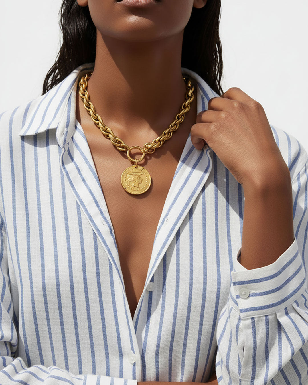 Model wearing a gold chunky chain necklace with a large Athena coin pendant.