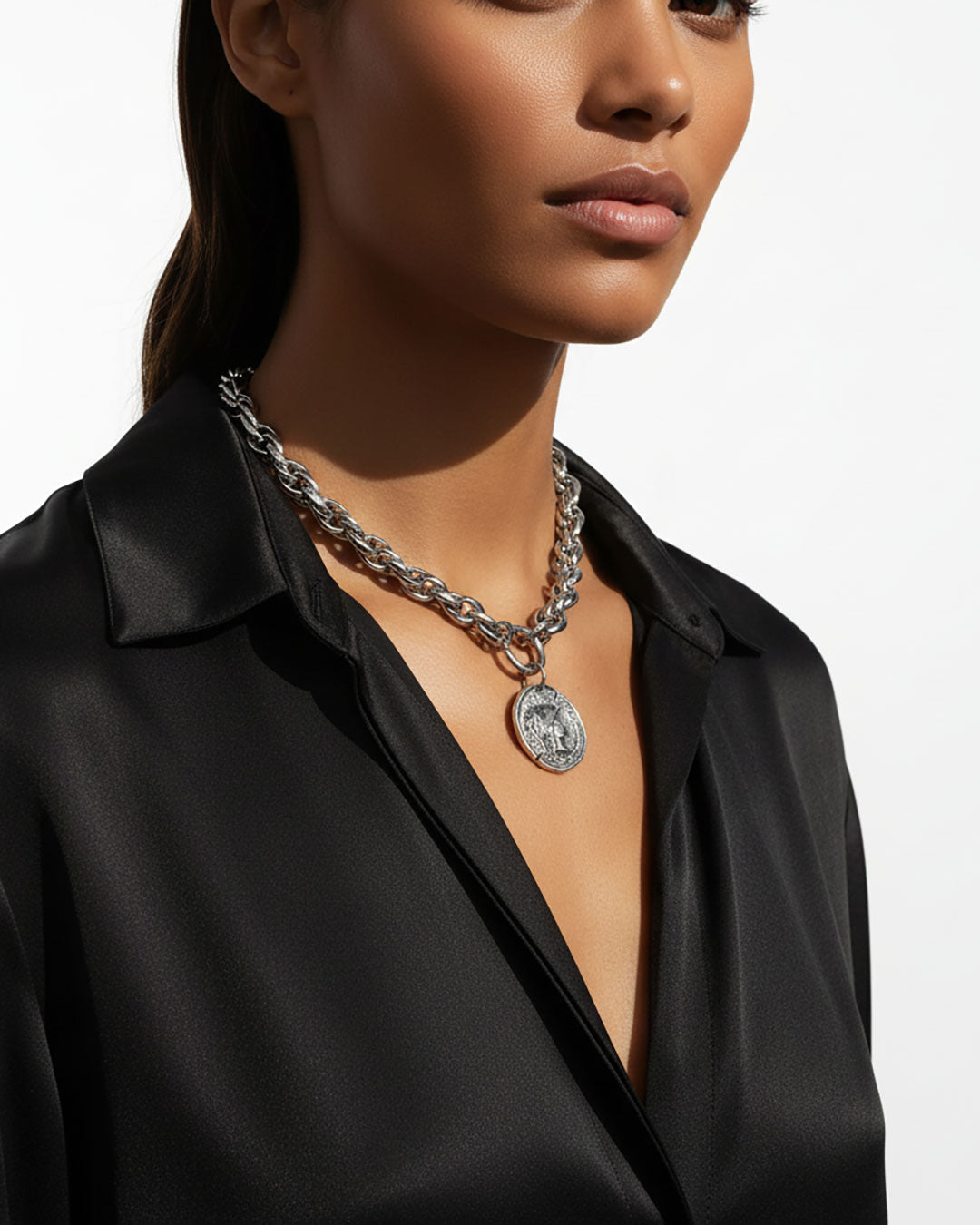 Model wearing a silver chunky chain necklace with a large Athena coin pendant.