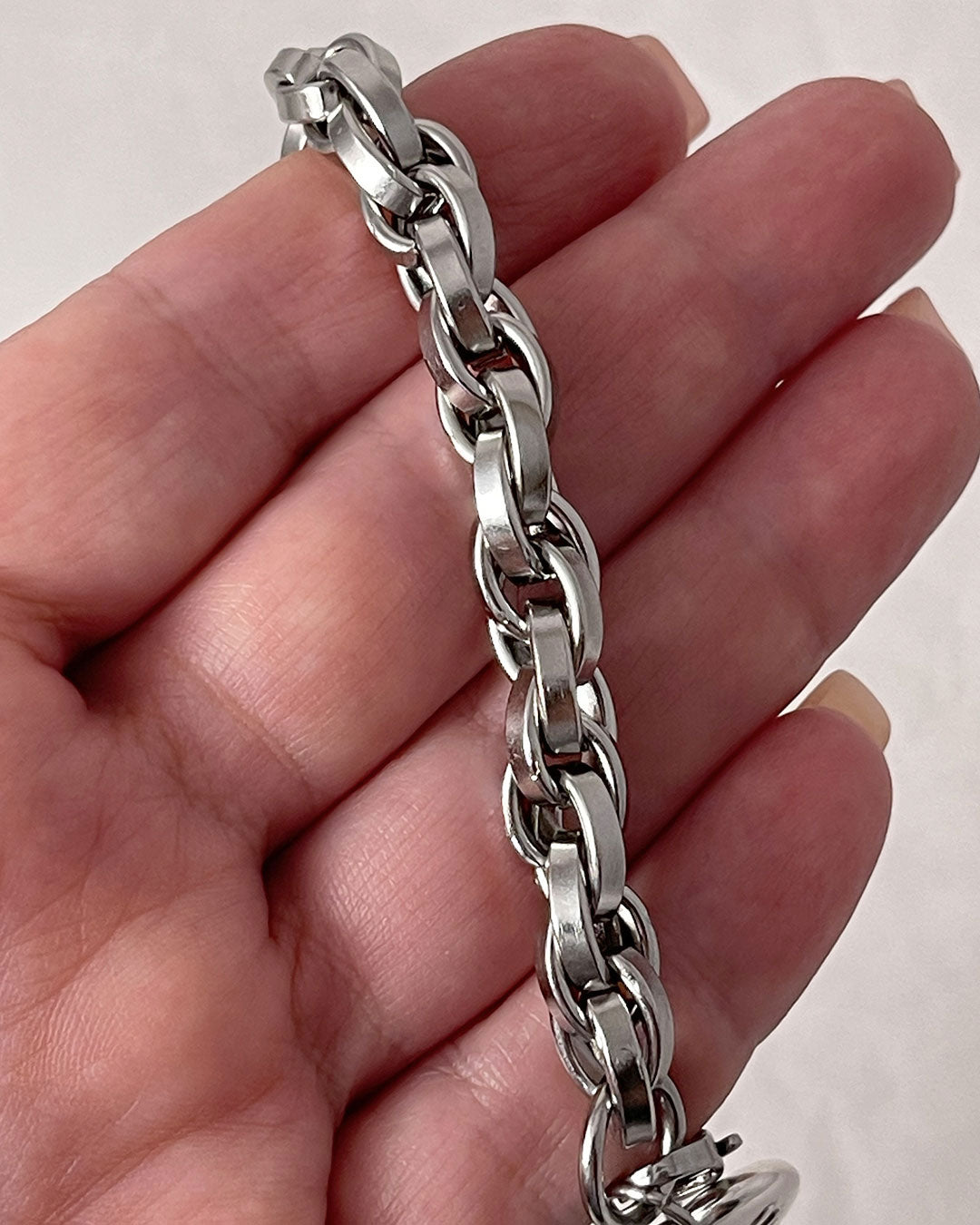 A hand holds a silver chain necklace against a neutral background. 