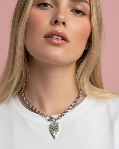 Model wearing a silver chain necklace with a heart-shaped pendant. The heart pendant has a raised eye design with sun rays around the eye.