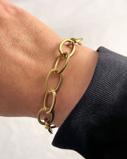 Chunky oval links chain bracelet in gold on a wrist with a plain background