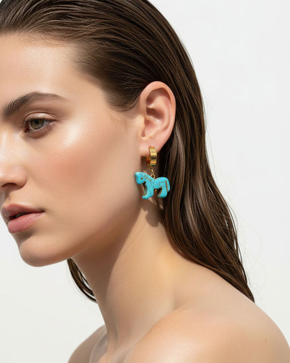 Model wearing turquoise horse-shaped earrings with gold hoops