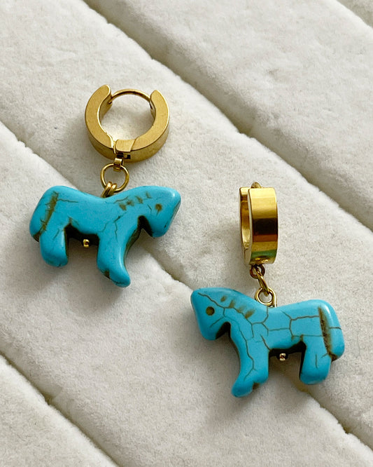 Turquoise horse-shaped earrings with gold hoops on a white surface

