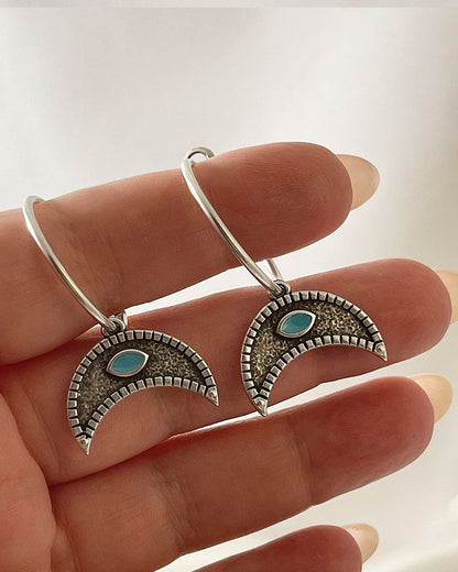The Crescent Horn Charm Hoop Earrings, a pair of silver hoop earrings featuring a crescent horn charm with a turquoise eye