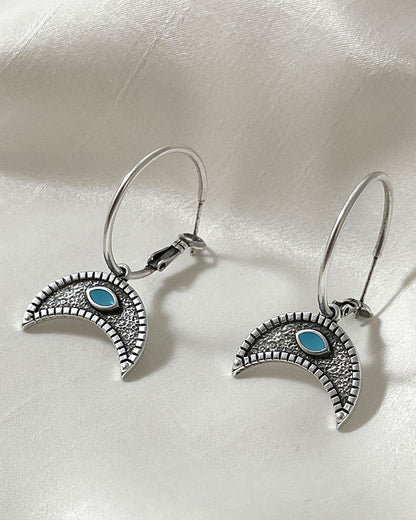 The Crescent Horn Charm Hoop Earrings, a pair of silver hoop earrings featuring a crescent horn charm with a turquoise eye