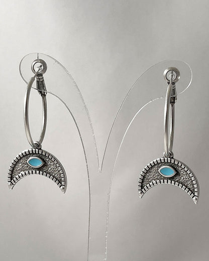 The Crescent Horn Charm Hoop Earrings, a pair of silver hoop earrings featuring a crescent horn charm with a turquoise eye