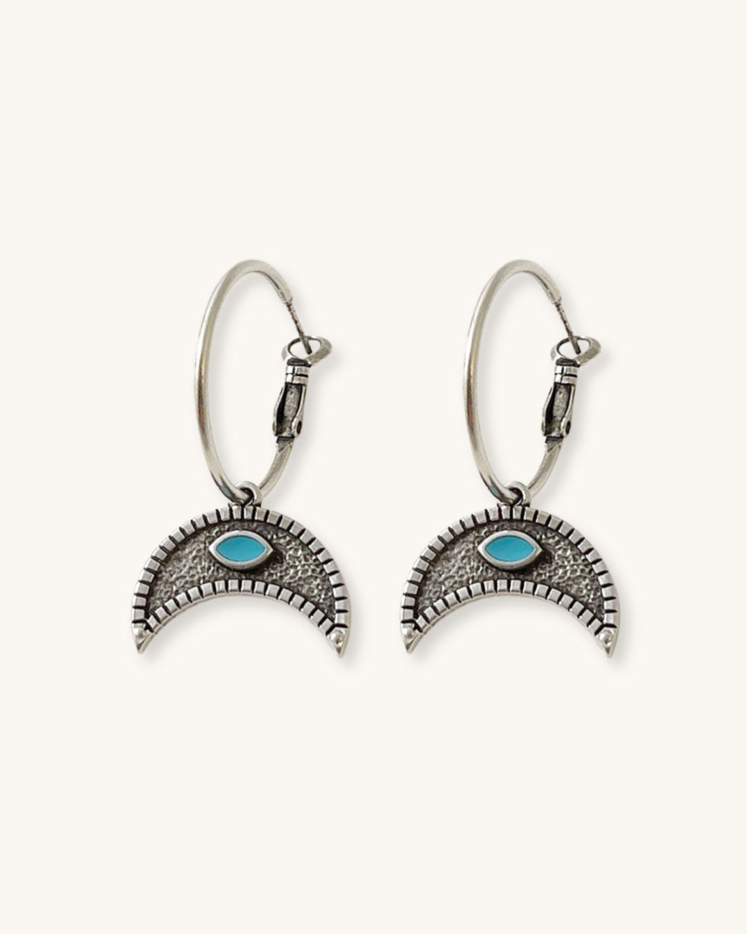 The Crescent Horn Charm Hoop Earrings, a pair of silver hoop earrings featuring a crescent horn charm with a turquoise eye