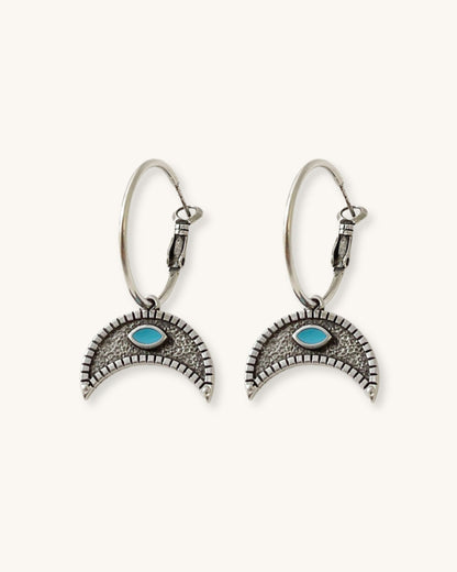 The Crescent Horn Charm Hoop Earrings, a pair of silver hoop earrings featuring a crescent horn charm with a turquoise eye