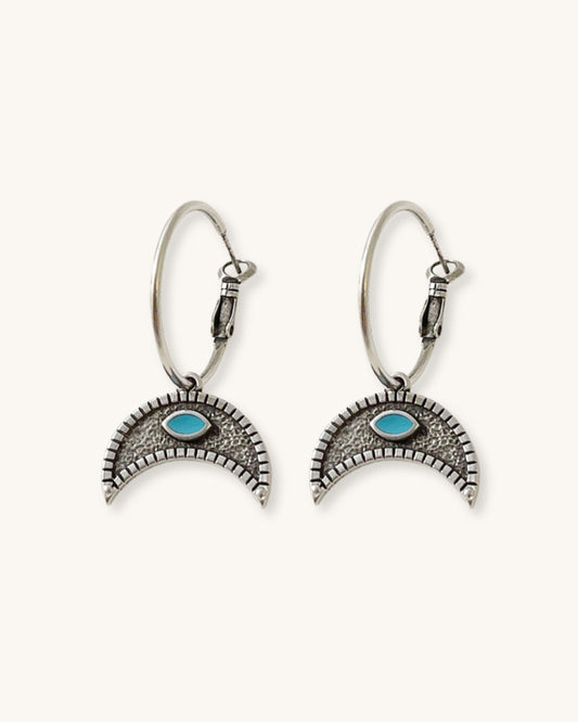 The Crescent Horn Charm Hoop Earrings, a pair of silver hoop earrings featuring a crescent horn charm with a turquoise eye