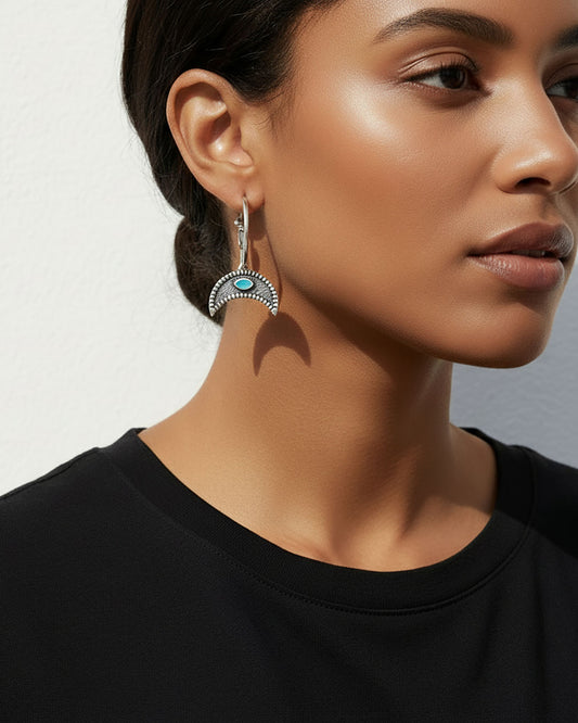 Model wearing a pair of silver hoop earrings featuring a crescent horn charm with a turquoise eye