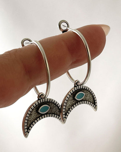 The Crescent Horn Charm Hoop Earrings, a pair of silver hoop earrings featuring a crescent horn charm with a turquoise eye