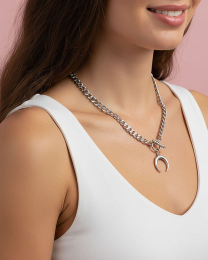 Woman wearing a silver chain necklace with a crescent moon pendant against a pink background