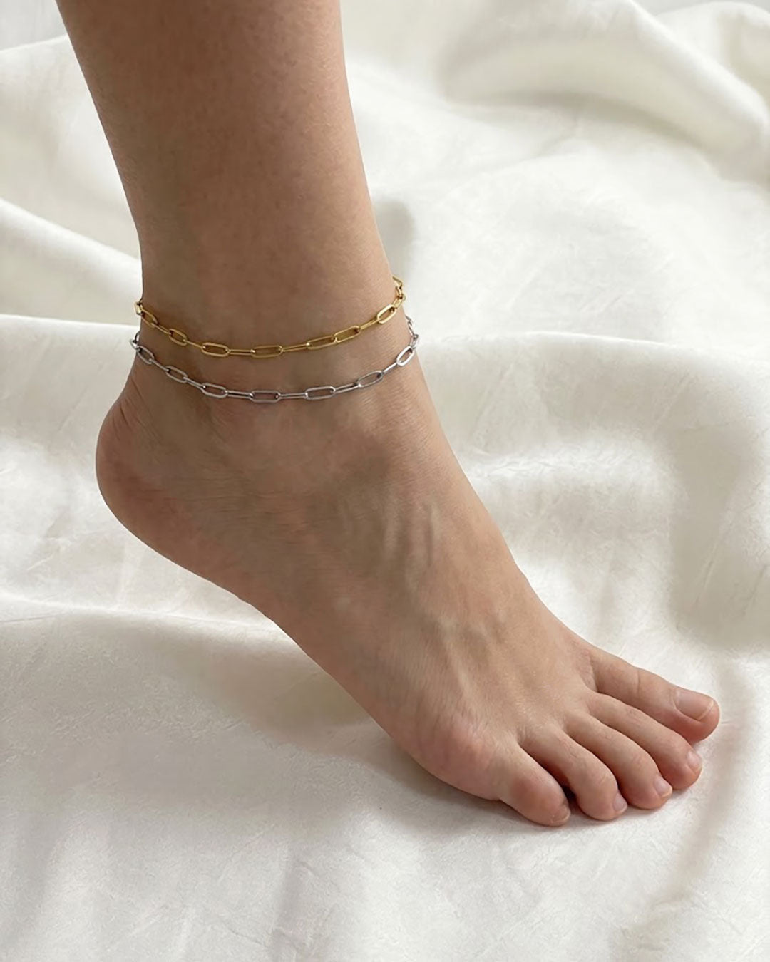 Two gold and silver paperclip chain amklets on a foot